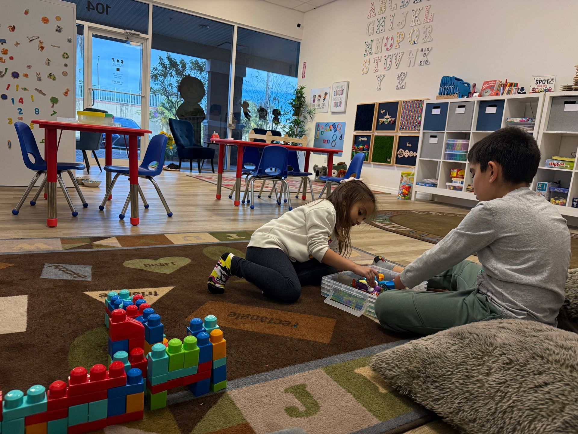 Two children playing with building blocks in a colorful classroom.