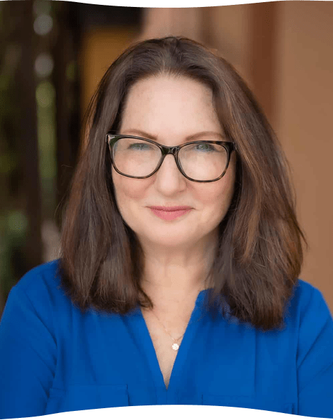 A woman wearing glasses and a blue shirt is smiling for the camera.