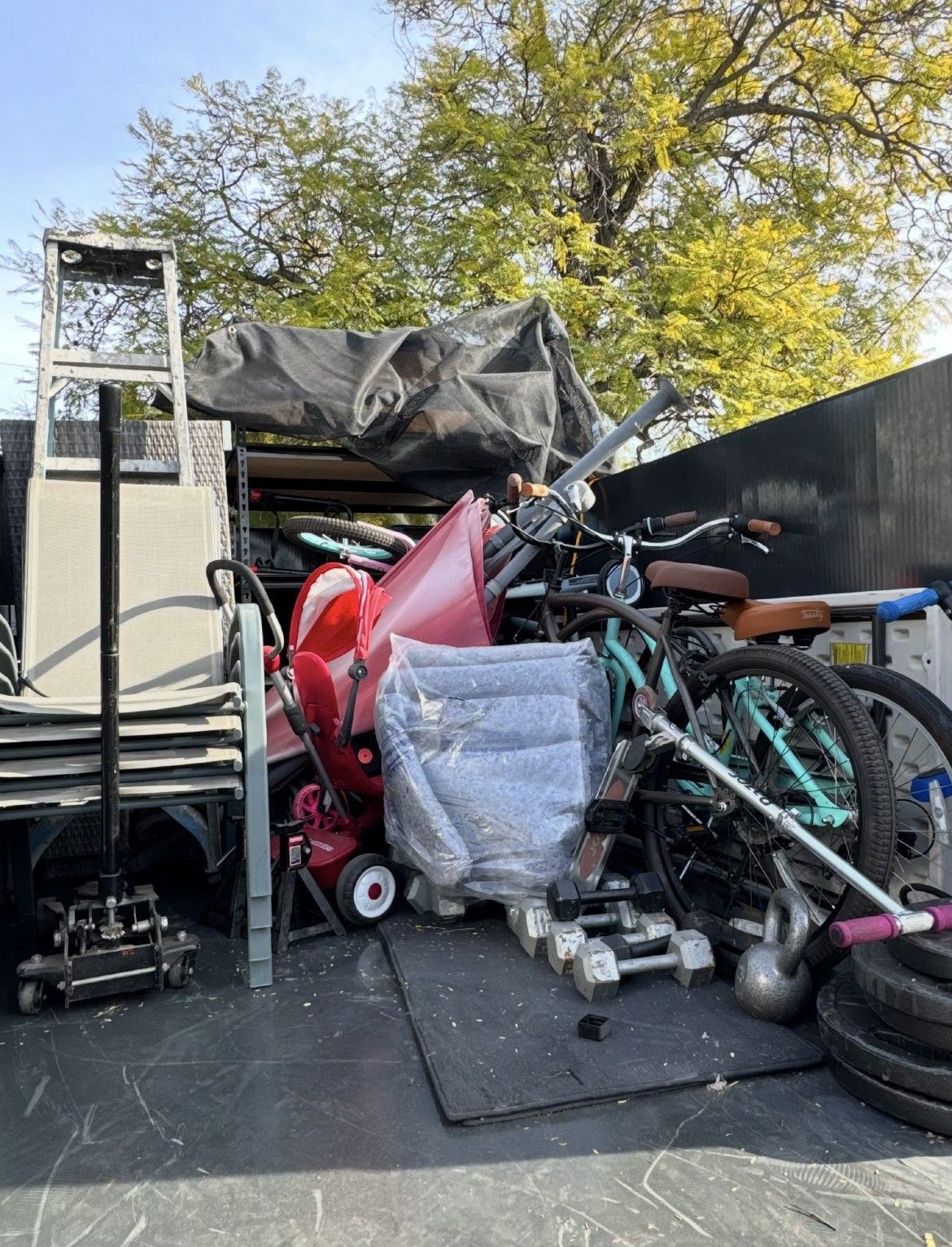 Truck bed filled with assorted items: a ladder, bicycle, weights, and tarp-covered objects.