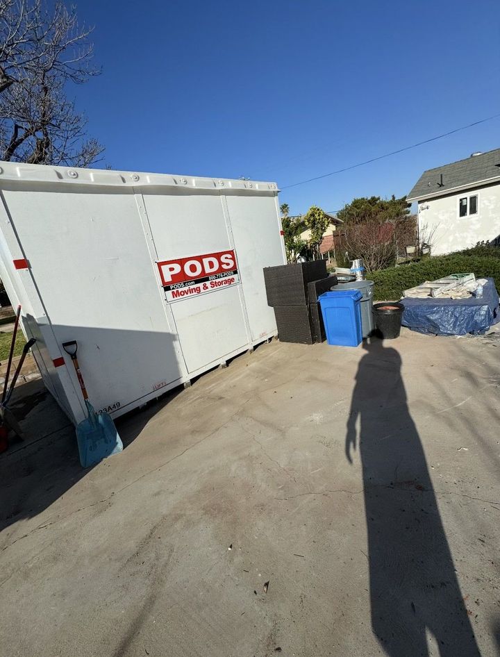 White PODS container in a driveway with debris and a person's shadow.
