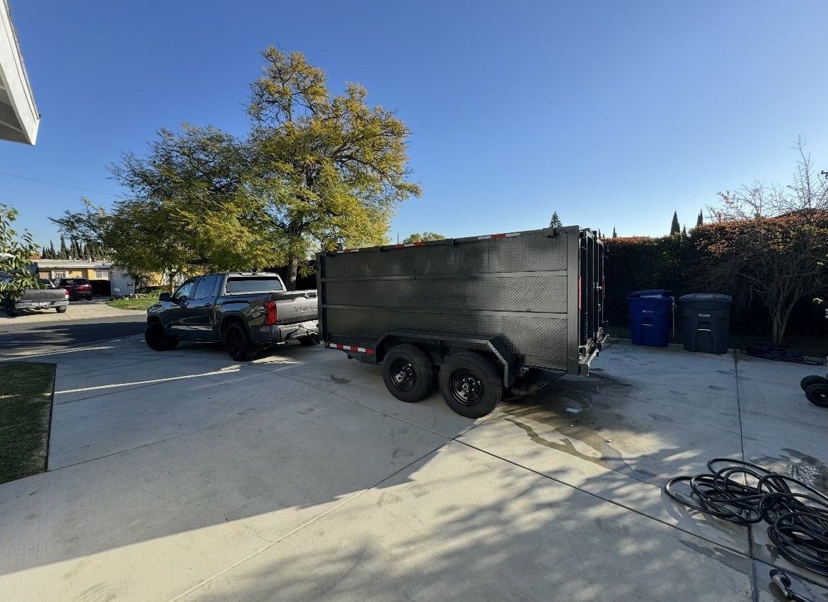 Truck towing a black enclosed trailer on a concrete driveway, under a clear, sunny sky.