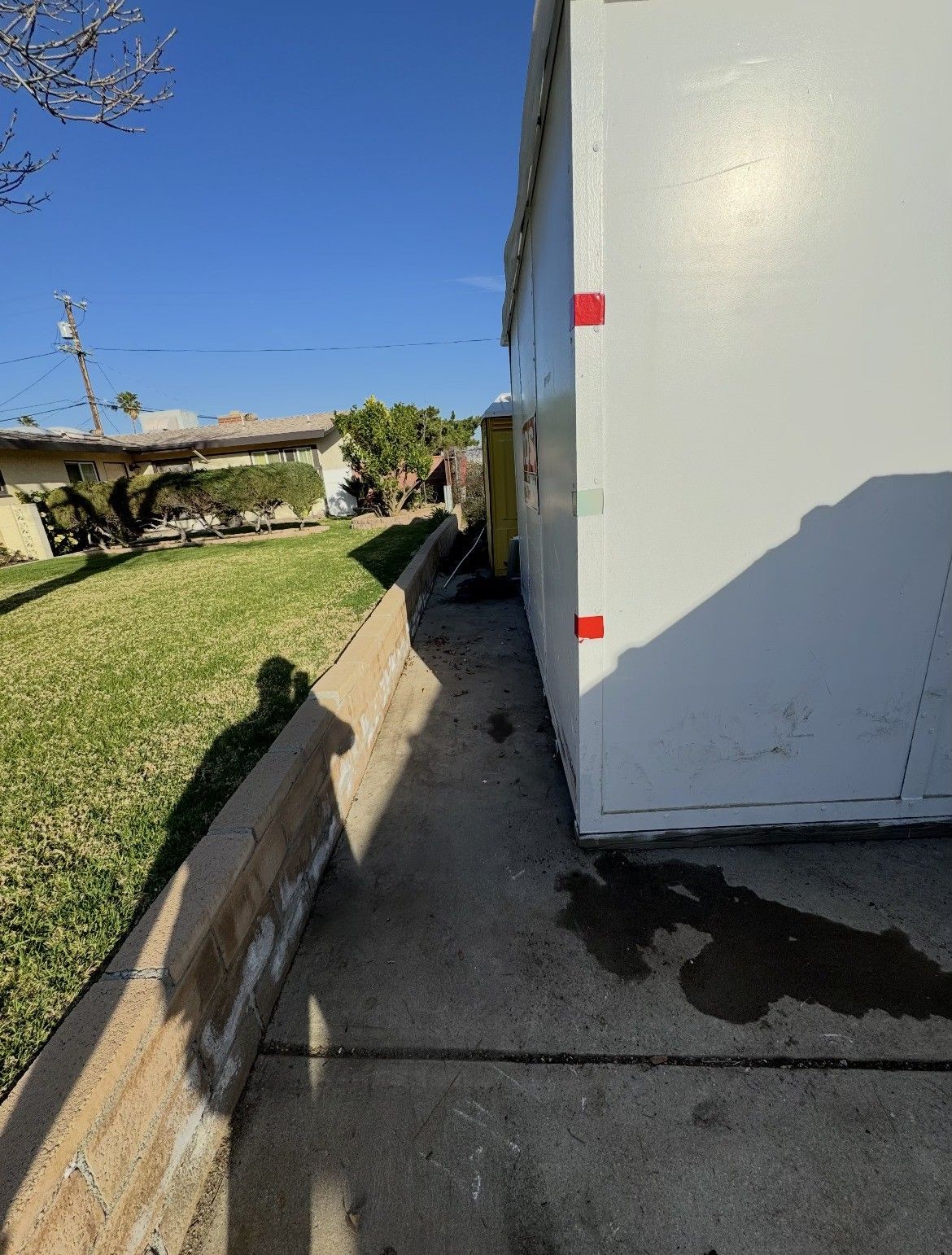 Sidewalk next to a white building. Grass, a low wall, and utility poles are in the background.