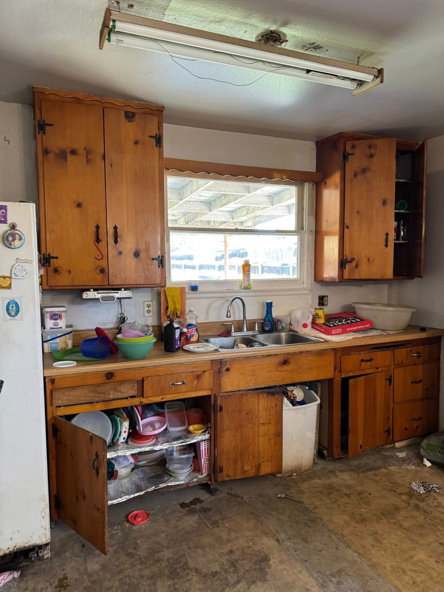 A cluttered kitchen with wooden cabinets, a sink, and a window.