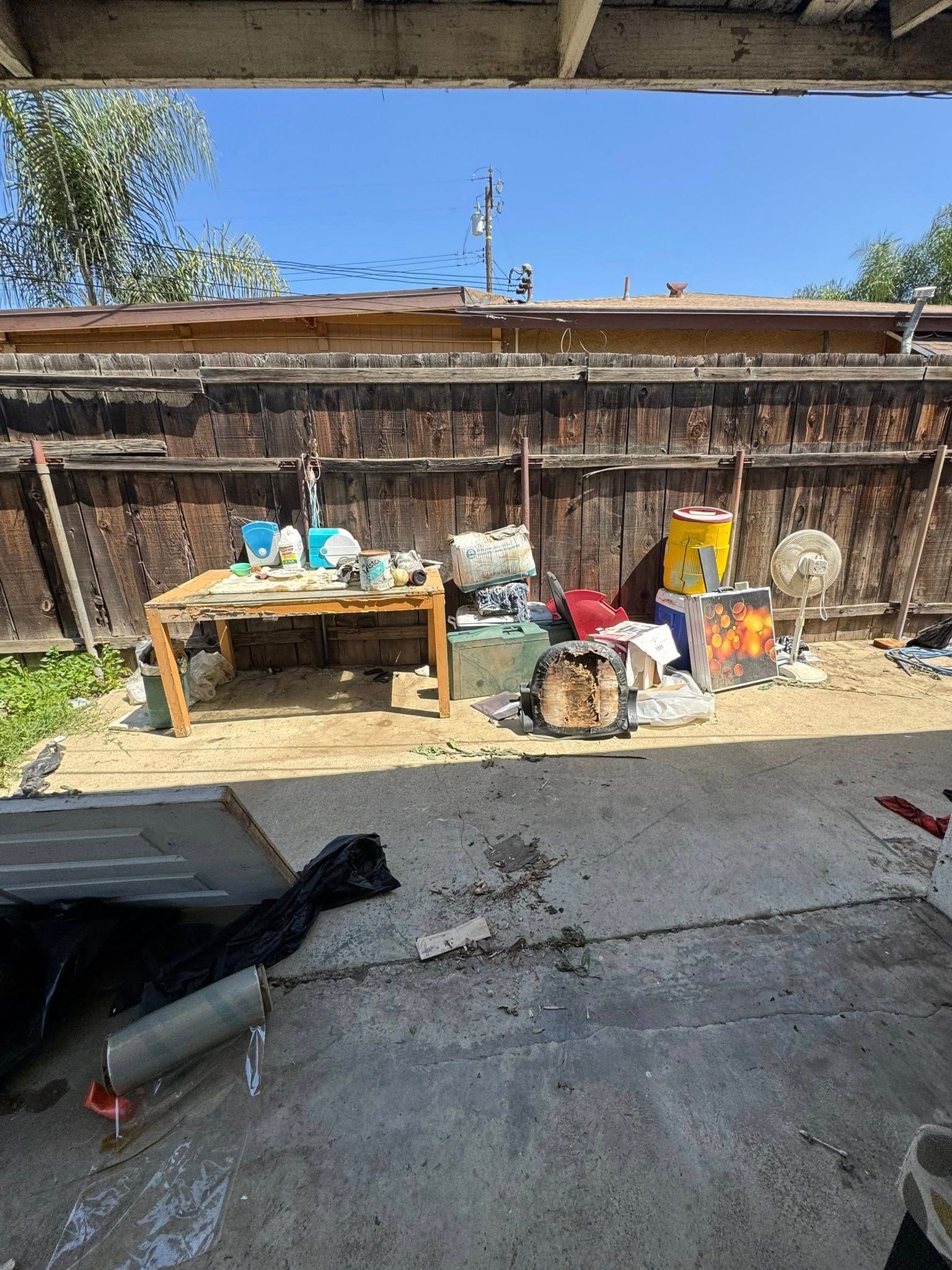 Backyard scene: a cluttered table, various items piled, wooden fence under a clear blue sky.