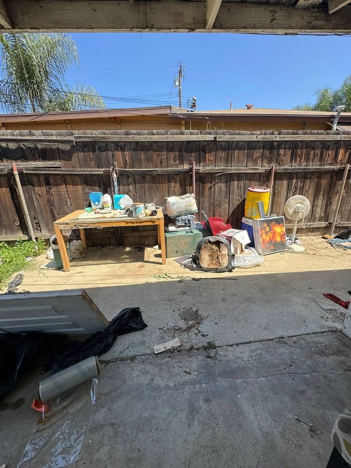 Backyard scene: a cluttered table, various items piled, wooden fence under a clear blue sky.