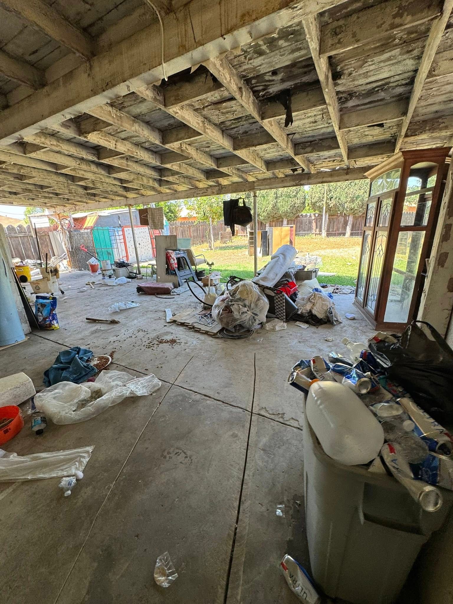 Messy outdoor area under a structure with debris scattered on the concrete floor.