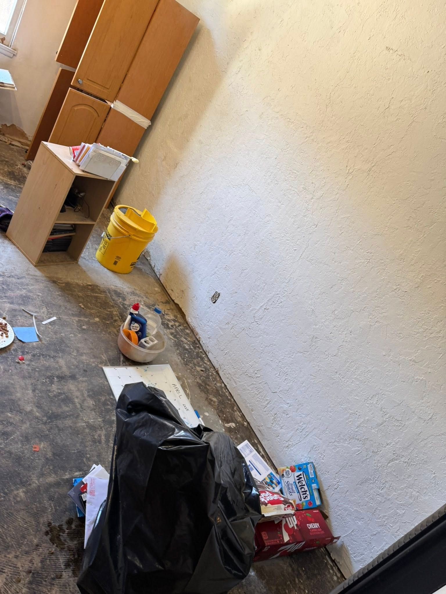 Messy room: cabinets, a bucket, and trash bags against a textured wall.