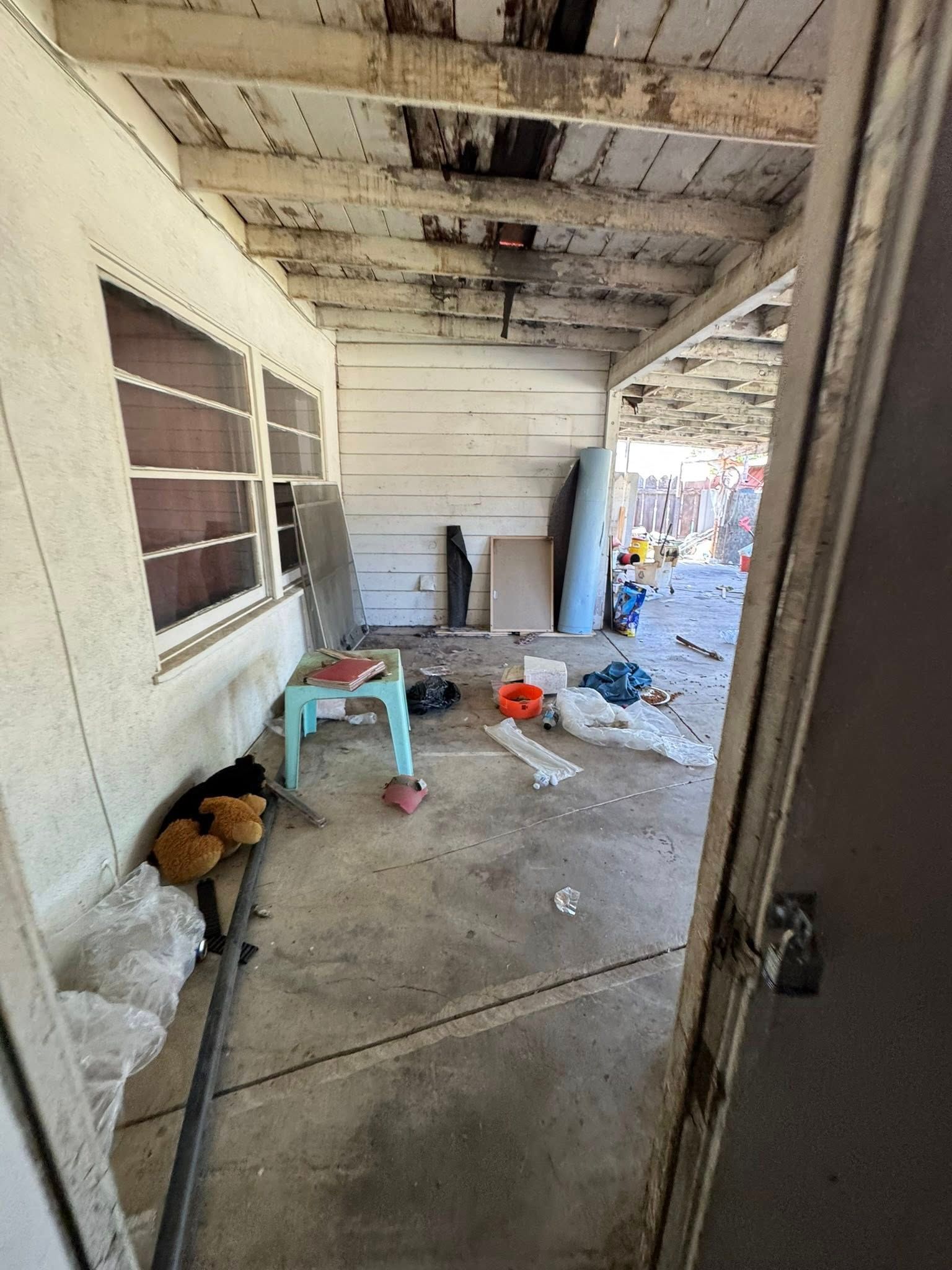 Dilapidated porch with debris, weathered ceiling, and windows.