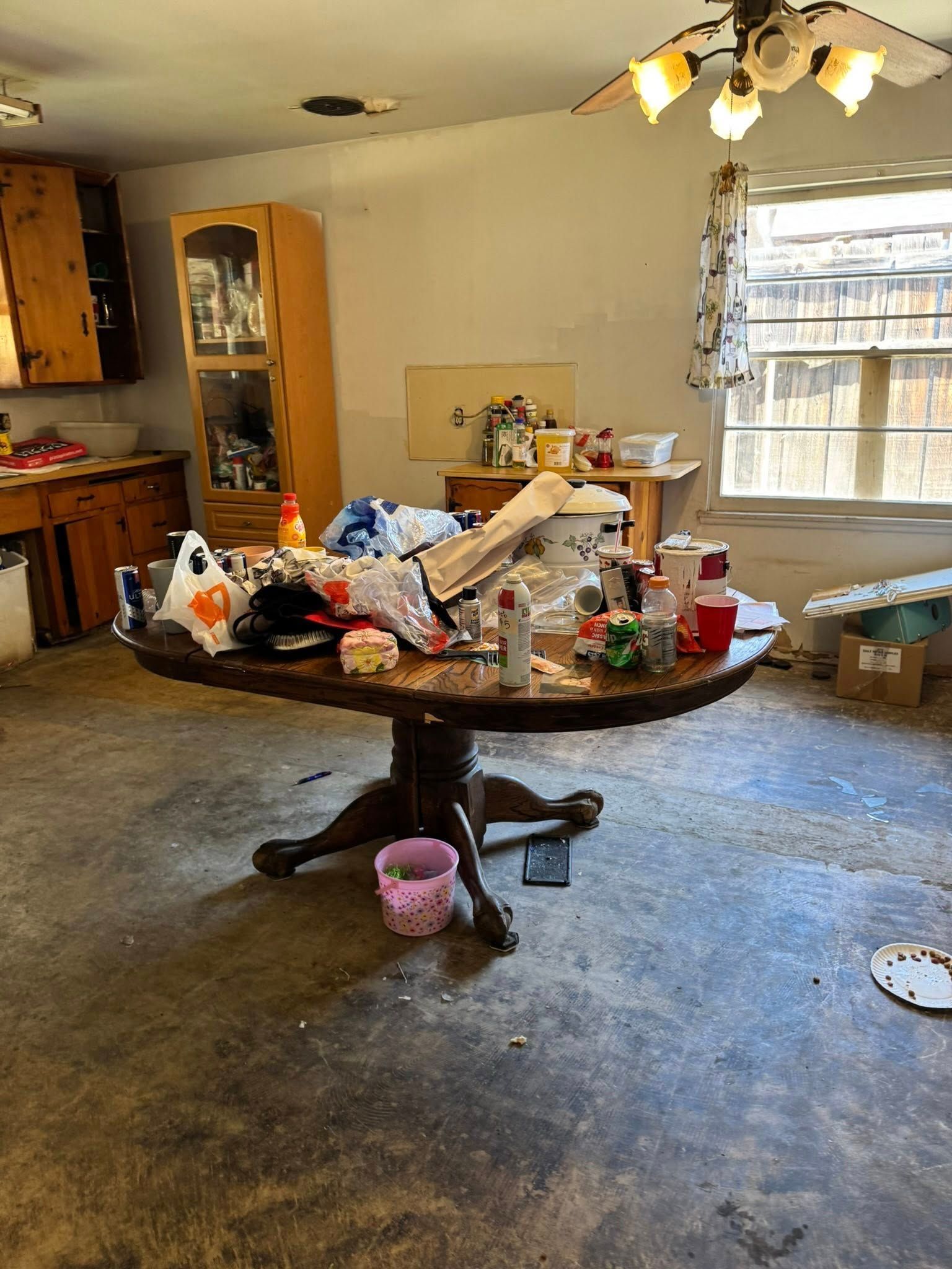 Messy kitchen with a cluttered round table, wooden cabinets, and a window with a view.