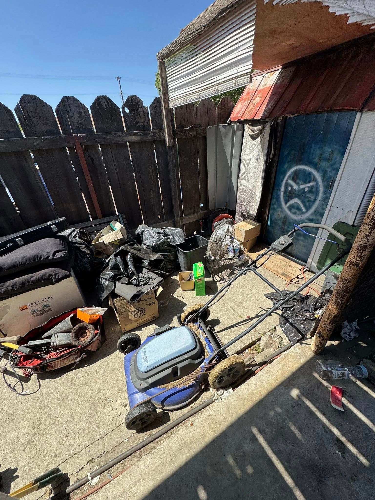 Yard with lawnmowers, trash, and a wooden fence. Overcast lighting.