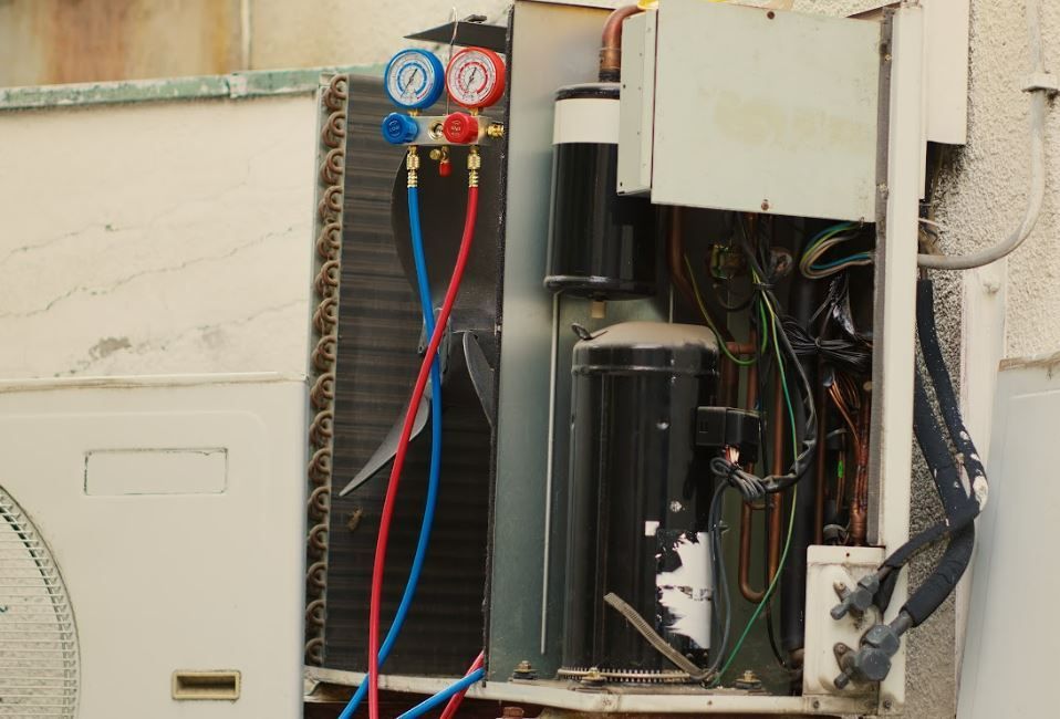 Outdoor HVAC unit with exposed wiring, blue and red gauges, and open panel cover