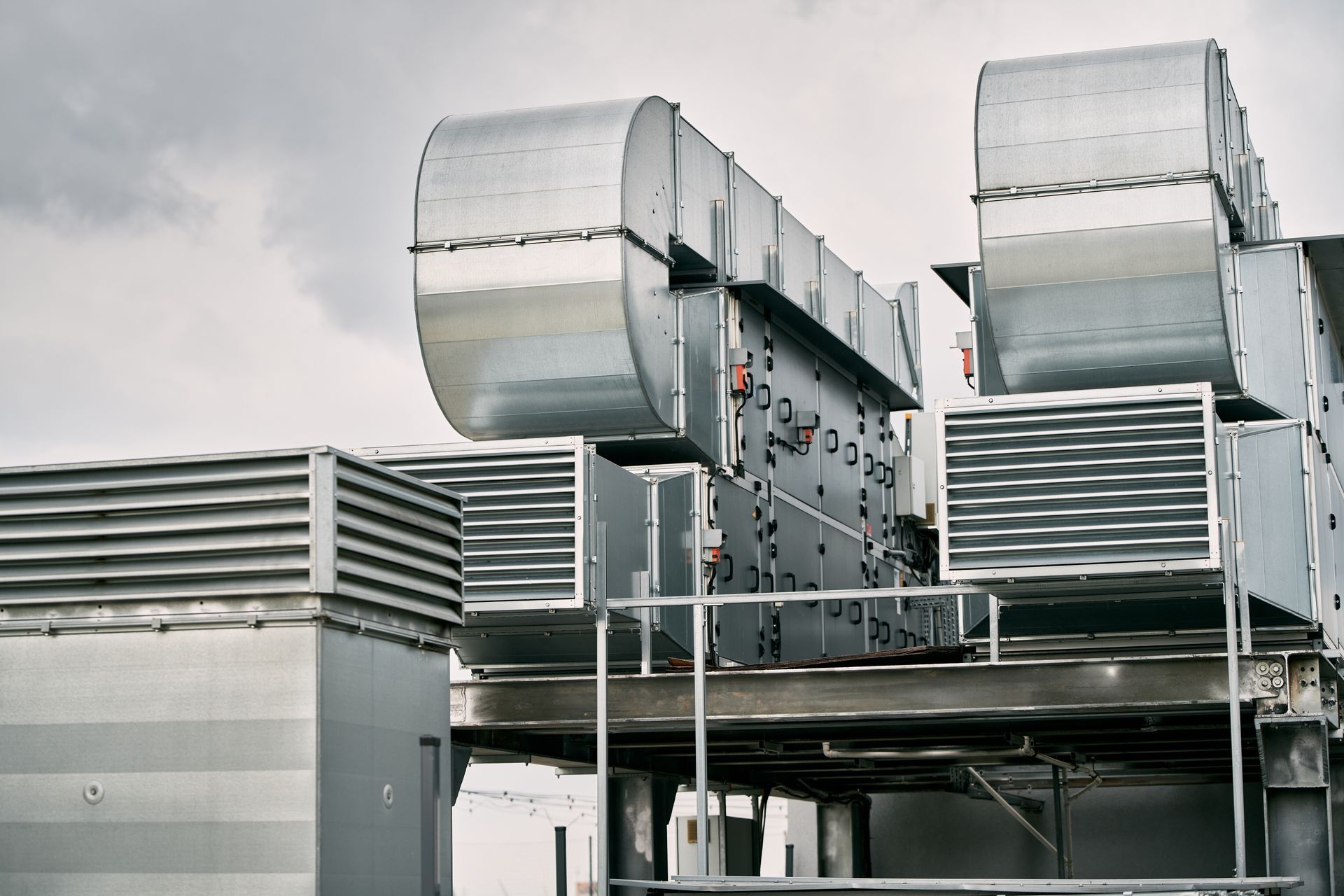 Rooftop industrial HVAC units and ventilation ducts on a metal platform under a cloudy sky