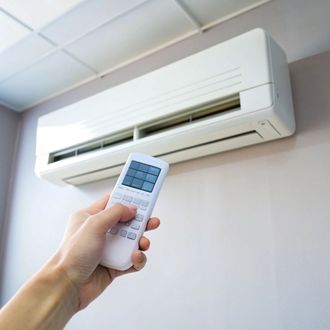 A person is holding a remote control in front of an air conditioner