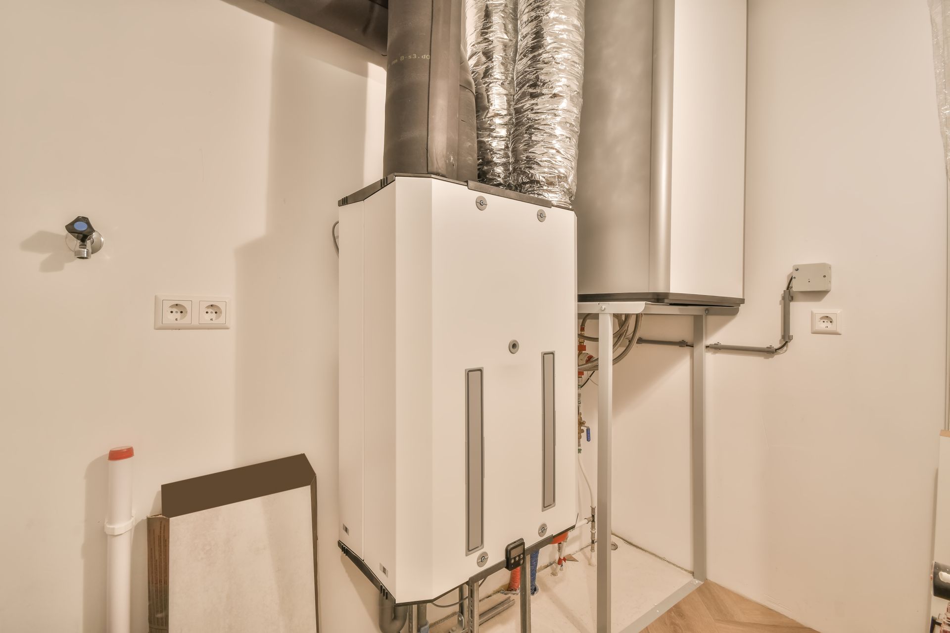 Wall-mounted HVAC/utility equipment with white cabinet, silver ducting, and pipes in a small room