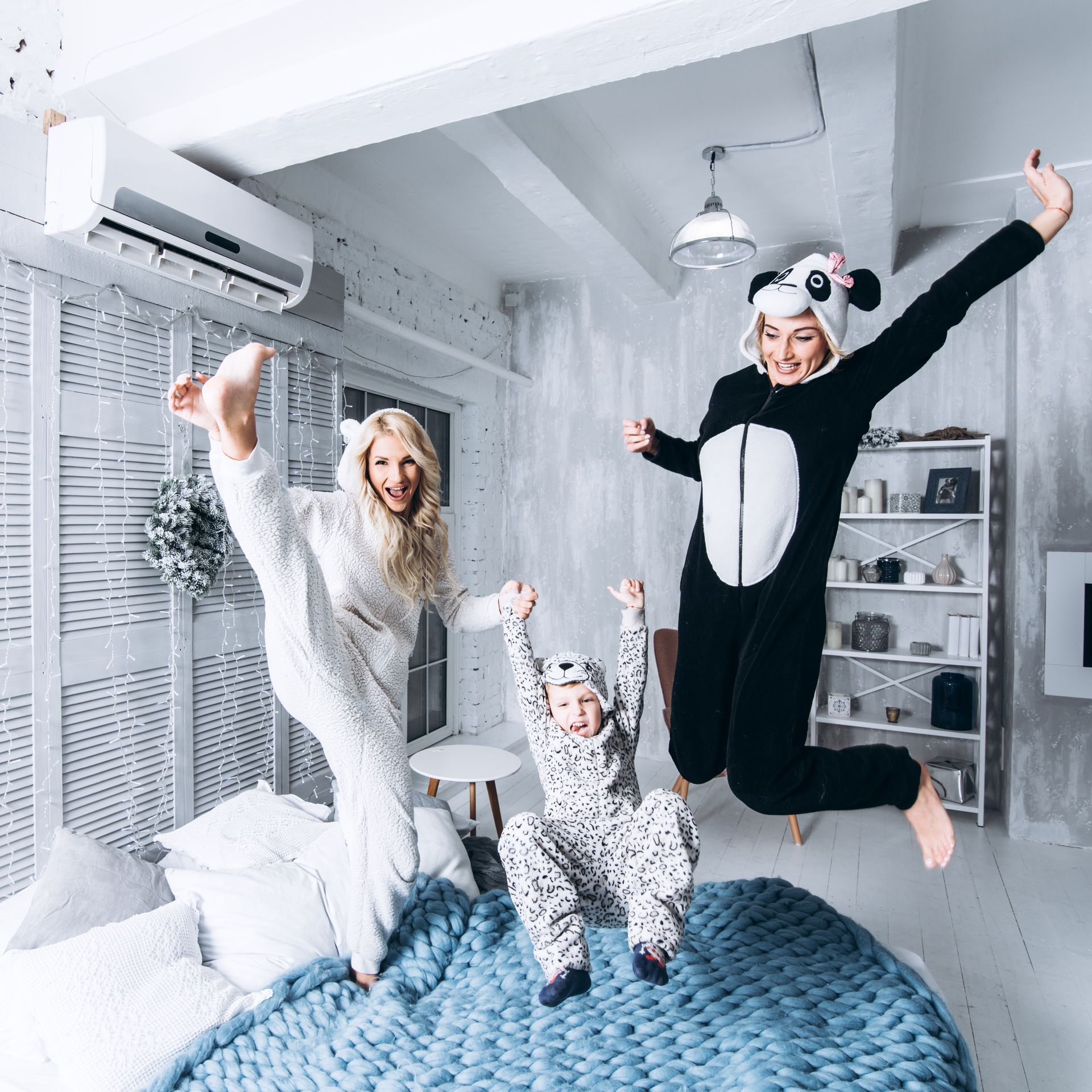 A woman in a panda costume is jumping in the air with a child on a bed.