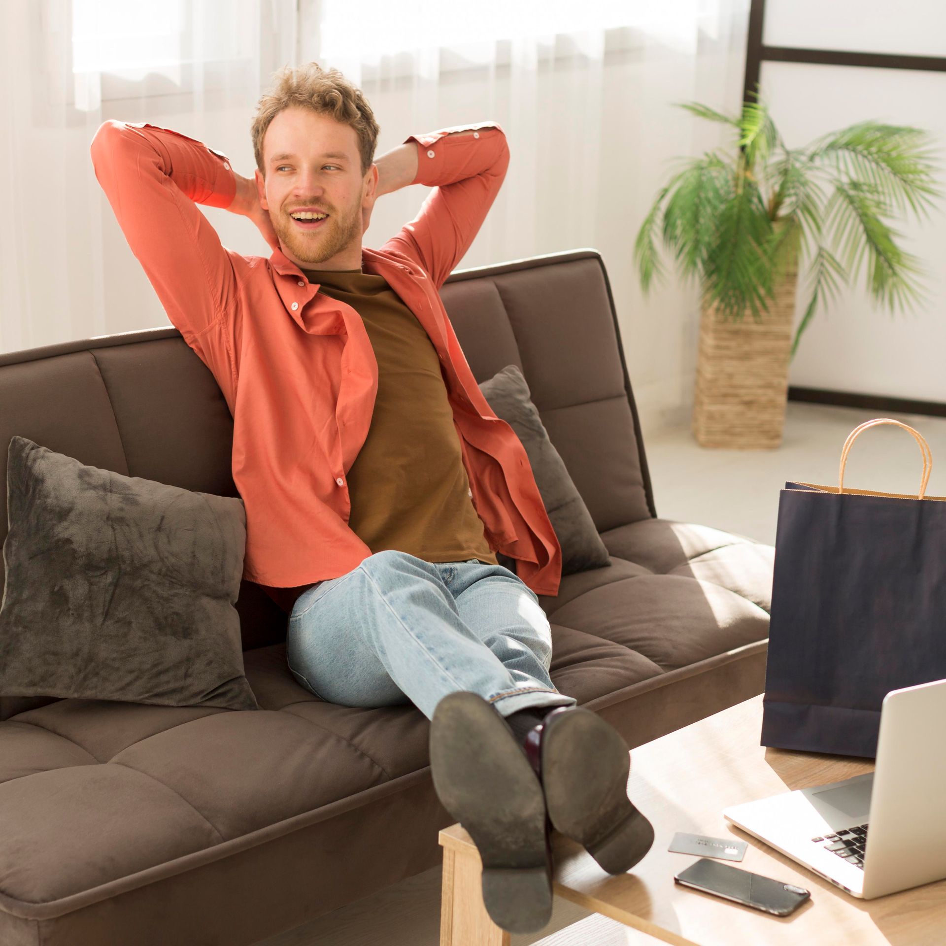 A man is sitting on a couch with his hands behind his head