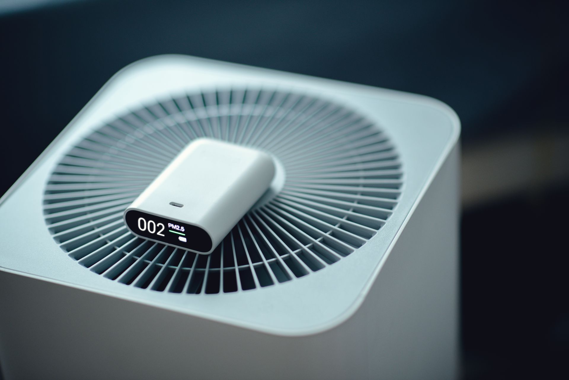 A small device is sitting on top of a white air purifier.