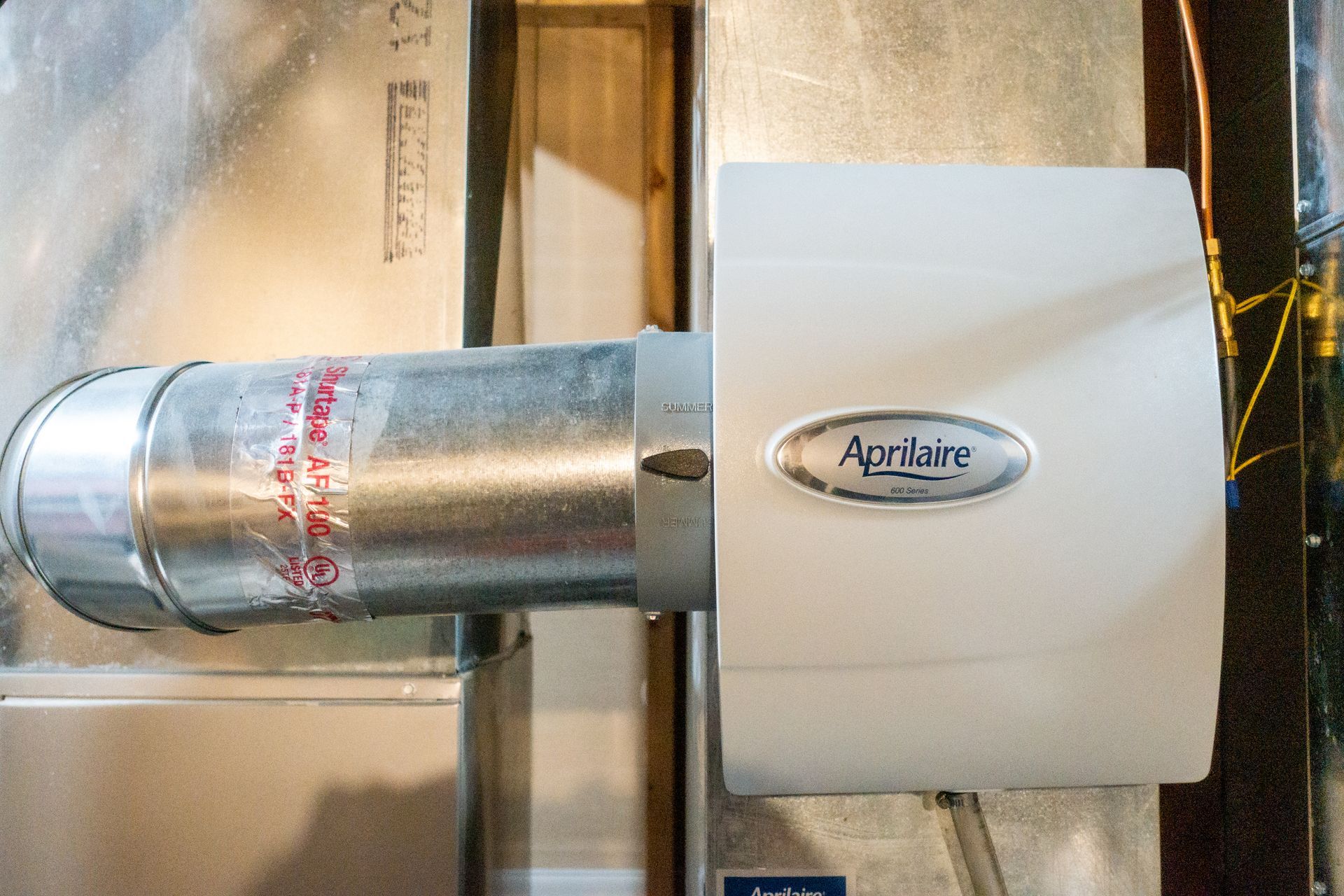 Aprilaire whole-house humidifier attached to HVAC ductwork. White unit with silver duct.