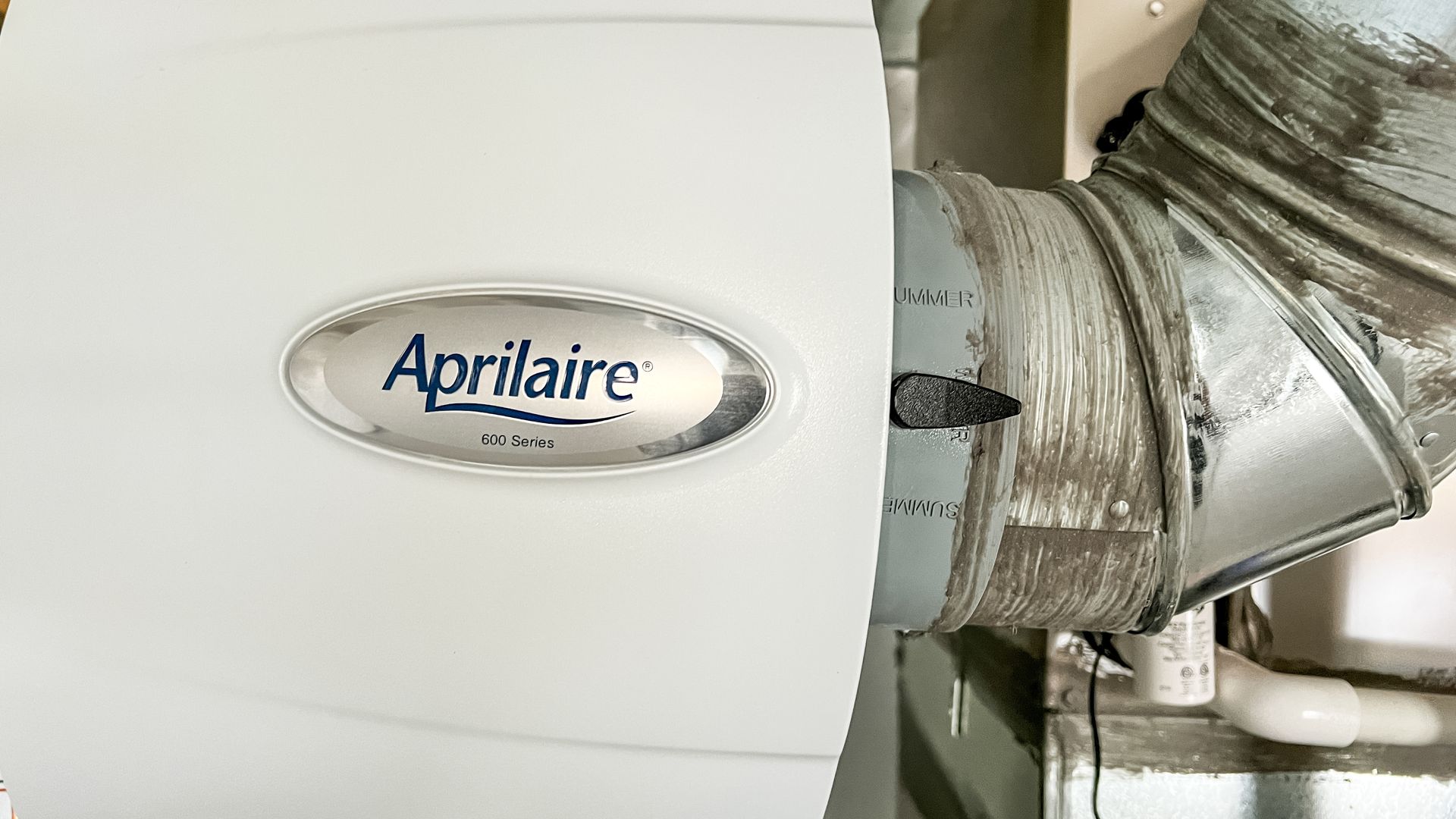Aprilaire humidifier attached to a duct, with the brand logo visible.