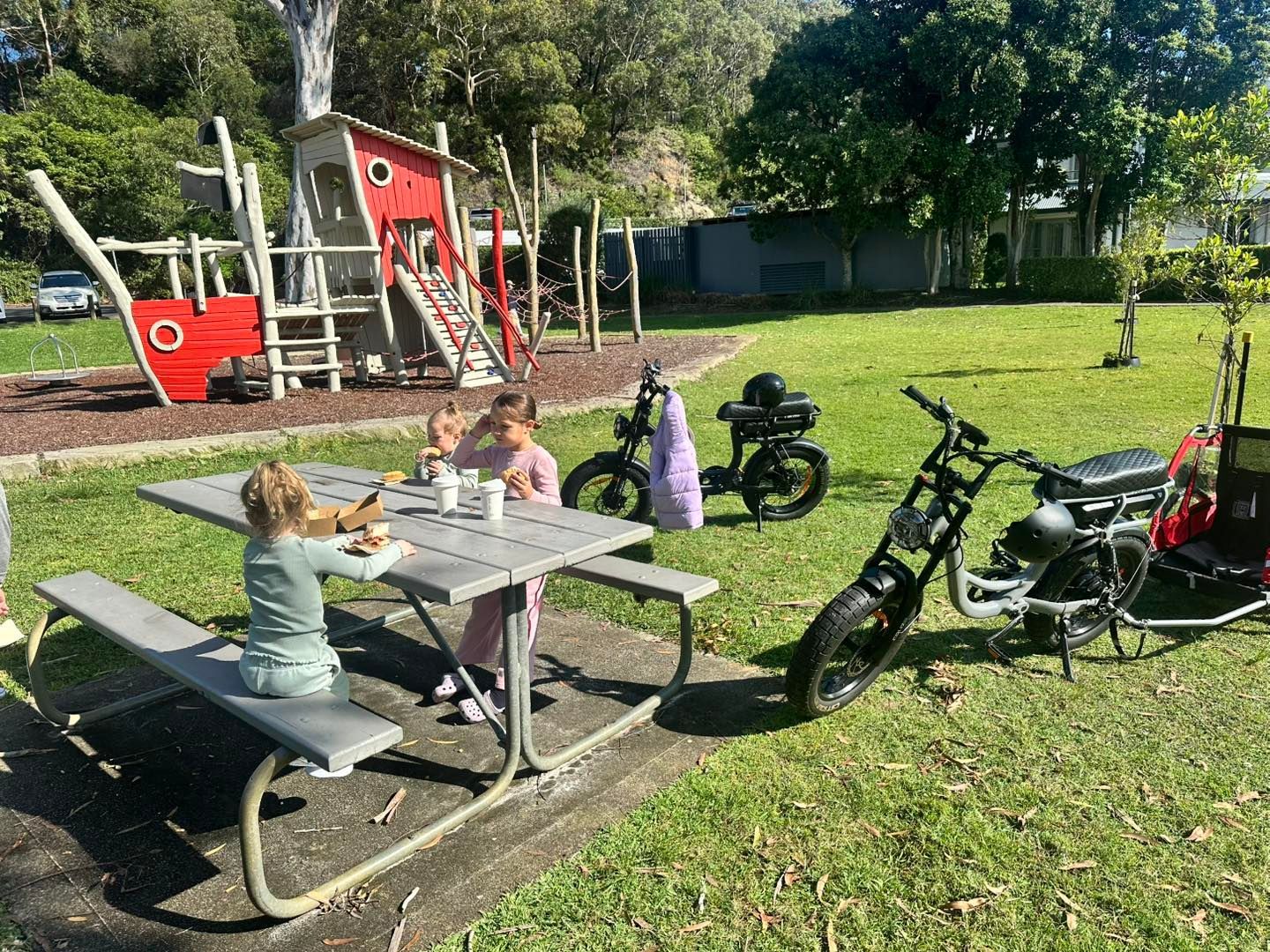 Two Children Sitting at A Picnic Table and Parked Electric Bicycles — E-Go-Try-Bikes in Nelson Bay, NSW