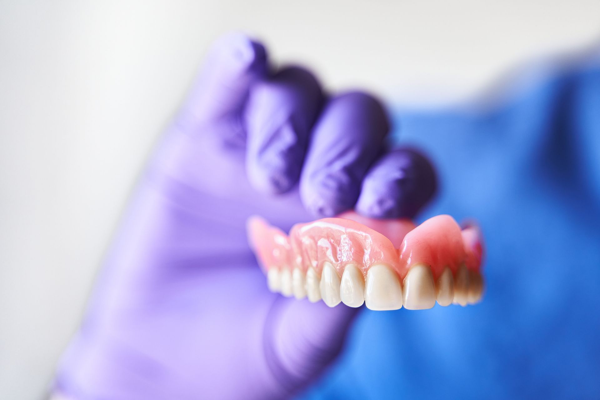 Close-up of a dentist with purple gloves, holding a denture in hand.