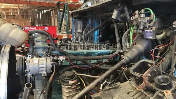 Blue semi-truck with the hood open in a repair shop, showing engine components.