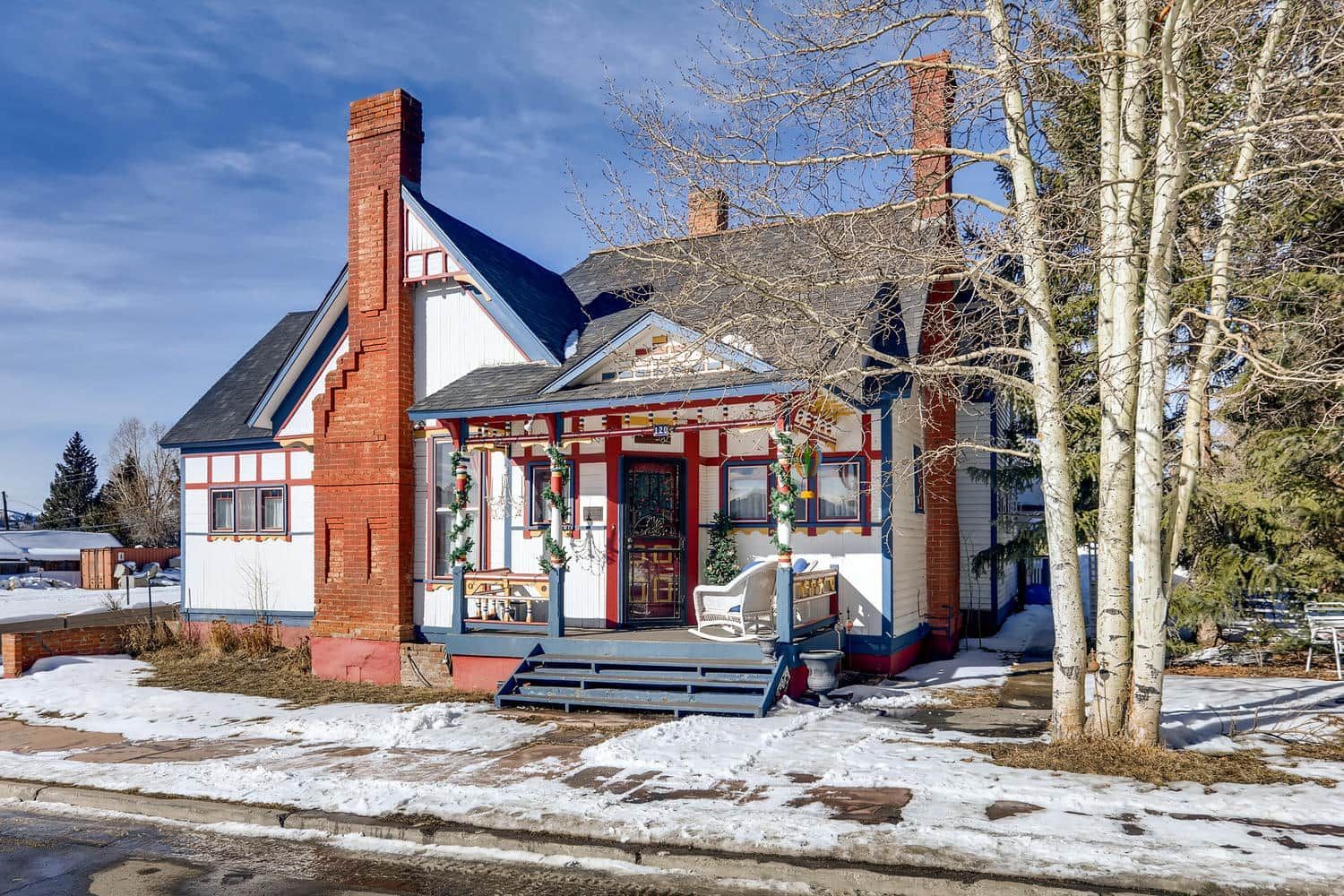 A house with a porch and a chimney is surrounded by snow and trees.