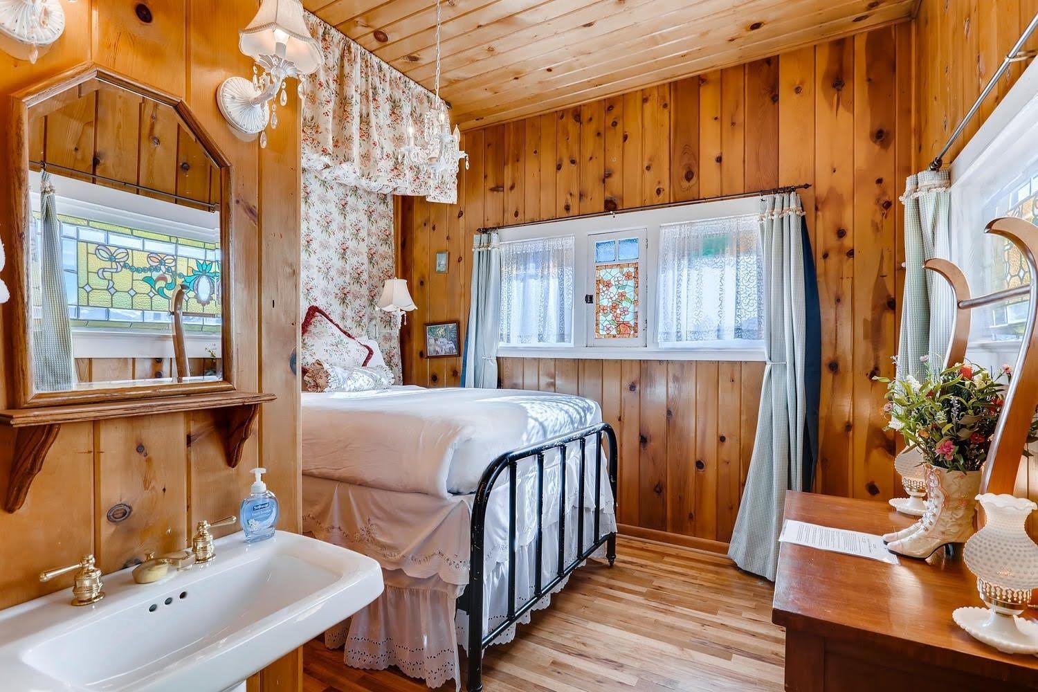 A bedroom with a bed , sink , mirror and stained glass window.