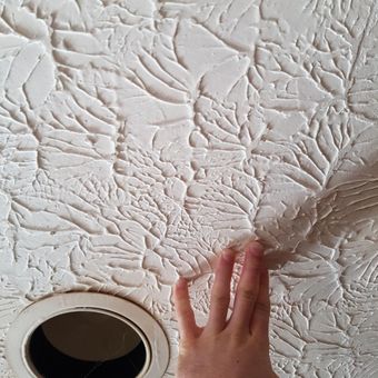 A person is touching a white ceiling with their hand.