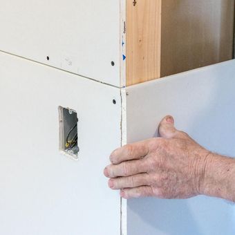 A person is holding a piece of drywall on a wall.