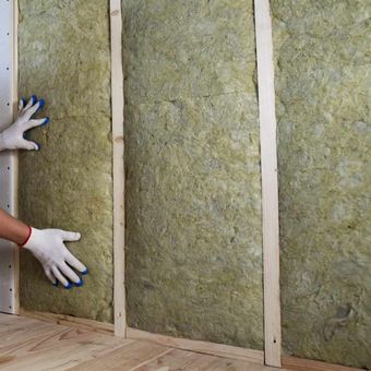 A person is holding a piece of rockwool on a wall.