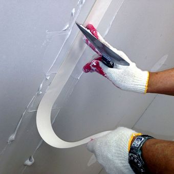 A person wearing gloves is holding a spatula and a roll of tape