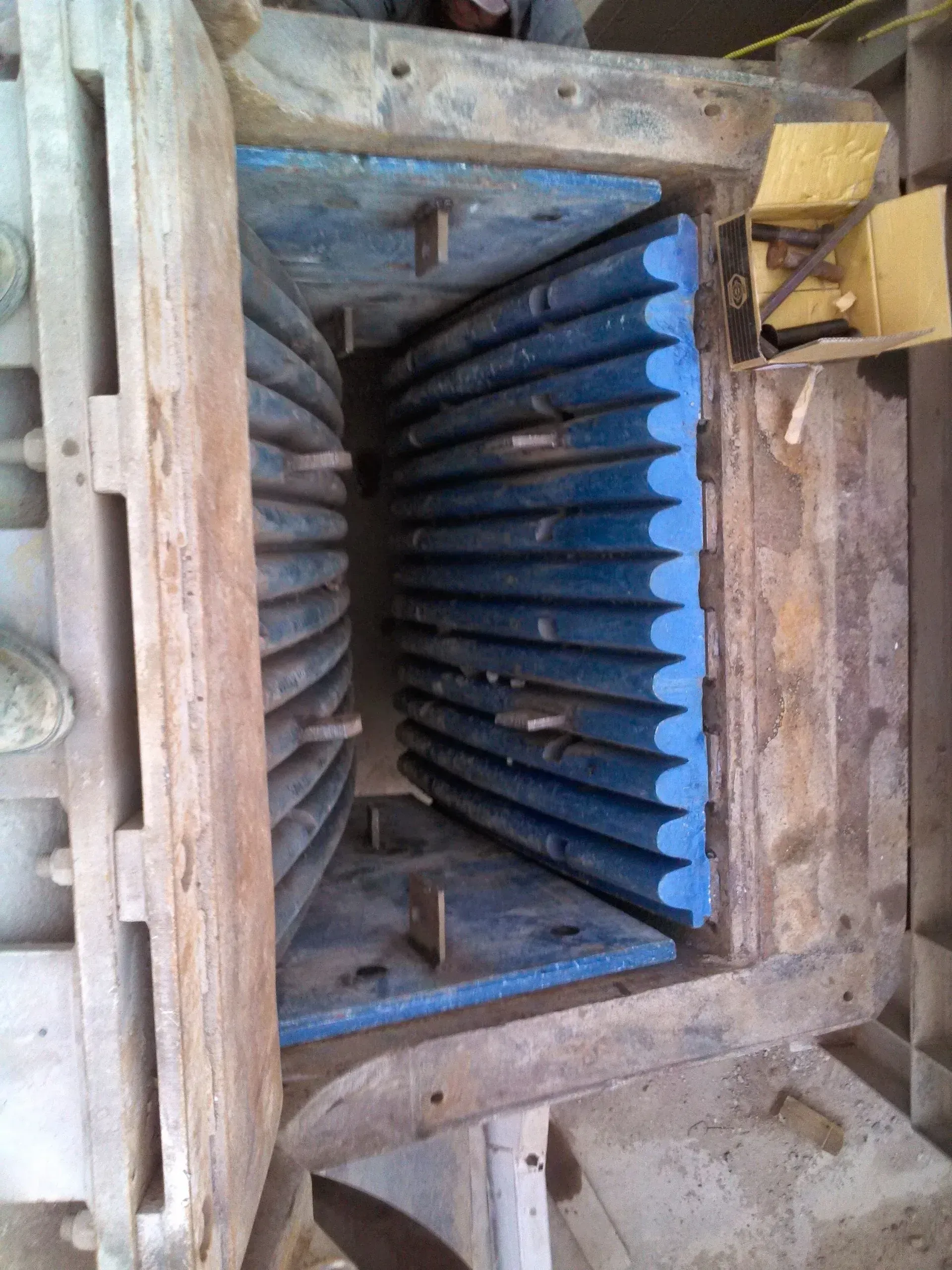 The inside of a machine with blue teeth and a wooden frame.