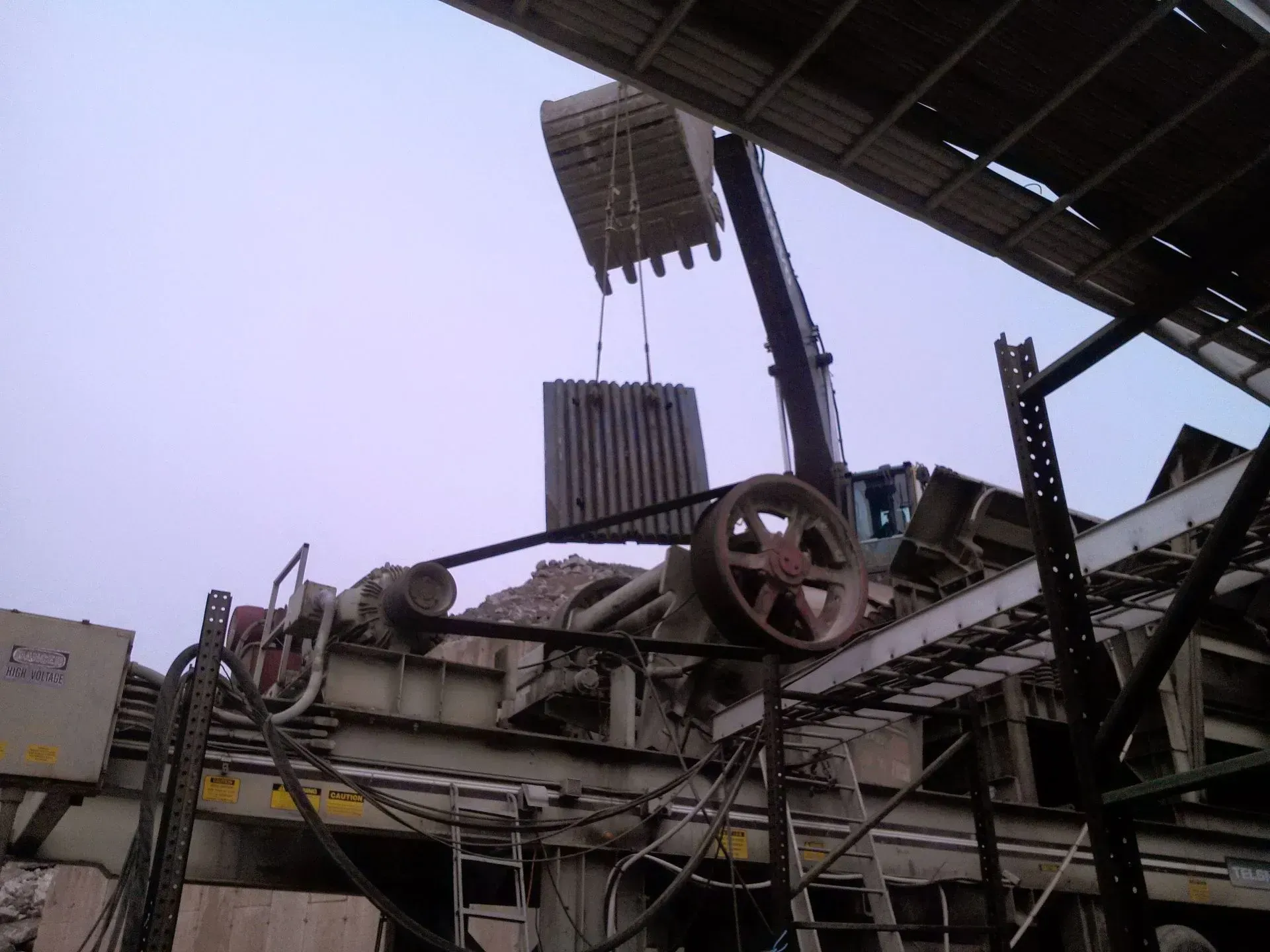 A crane is lifting a piece of metal from a conveyor belt.