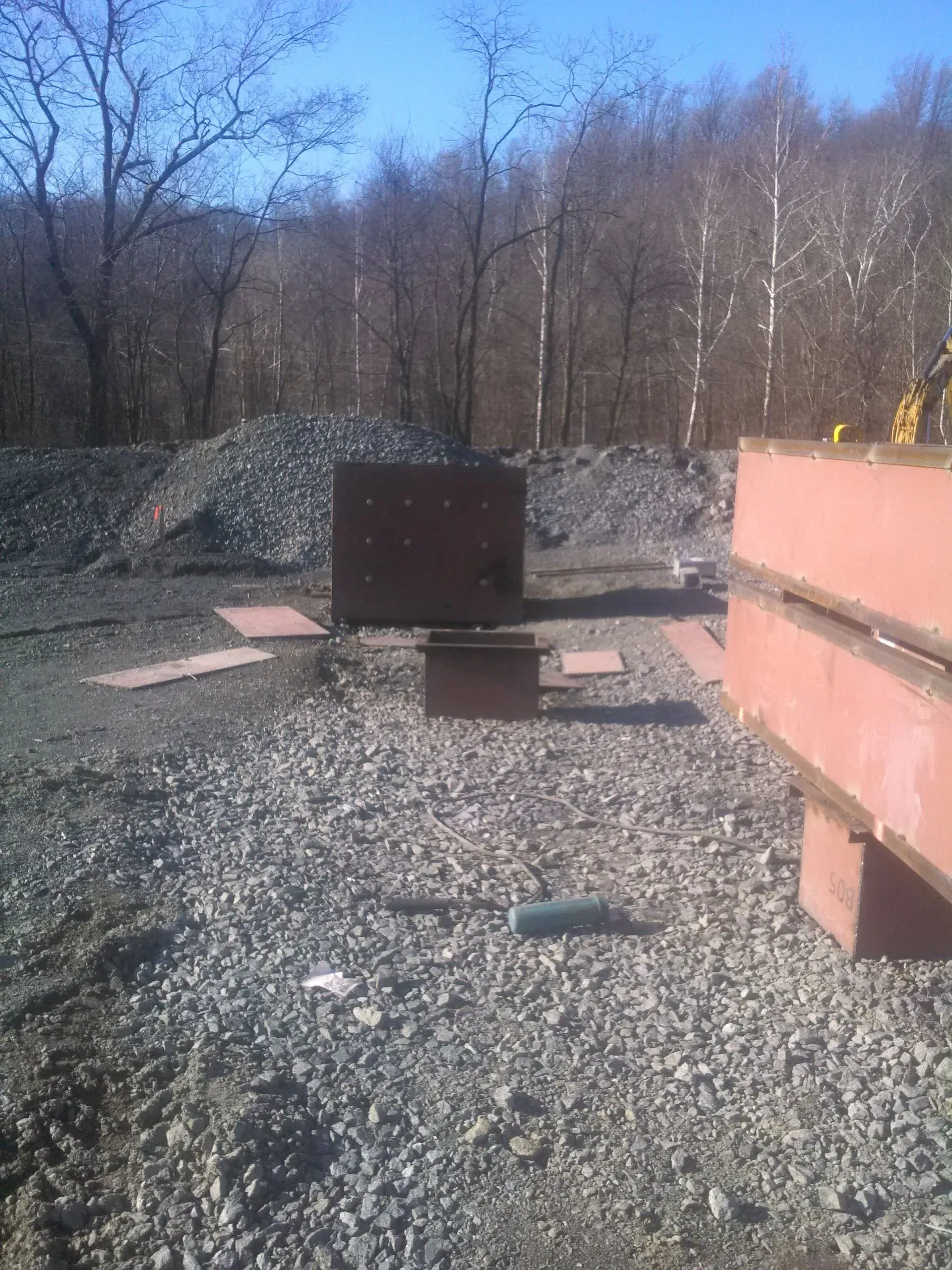 A gravel area with trees in the background and a bench in the foreground.