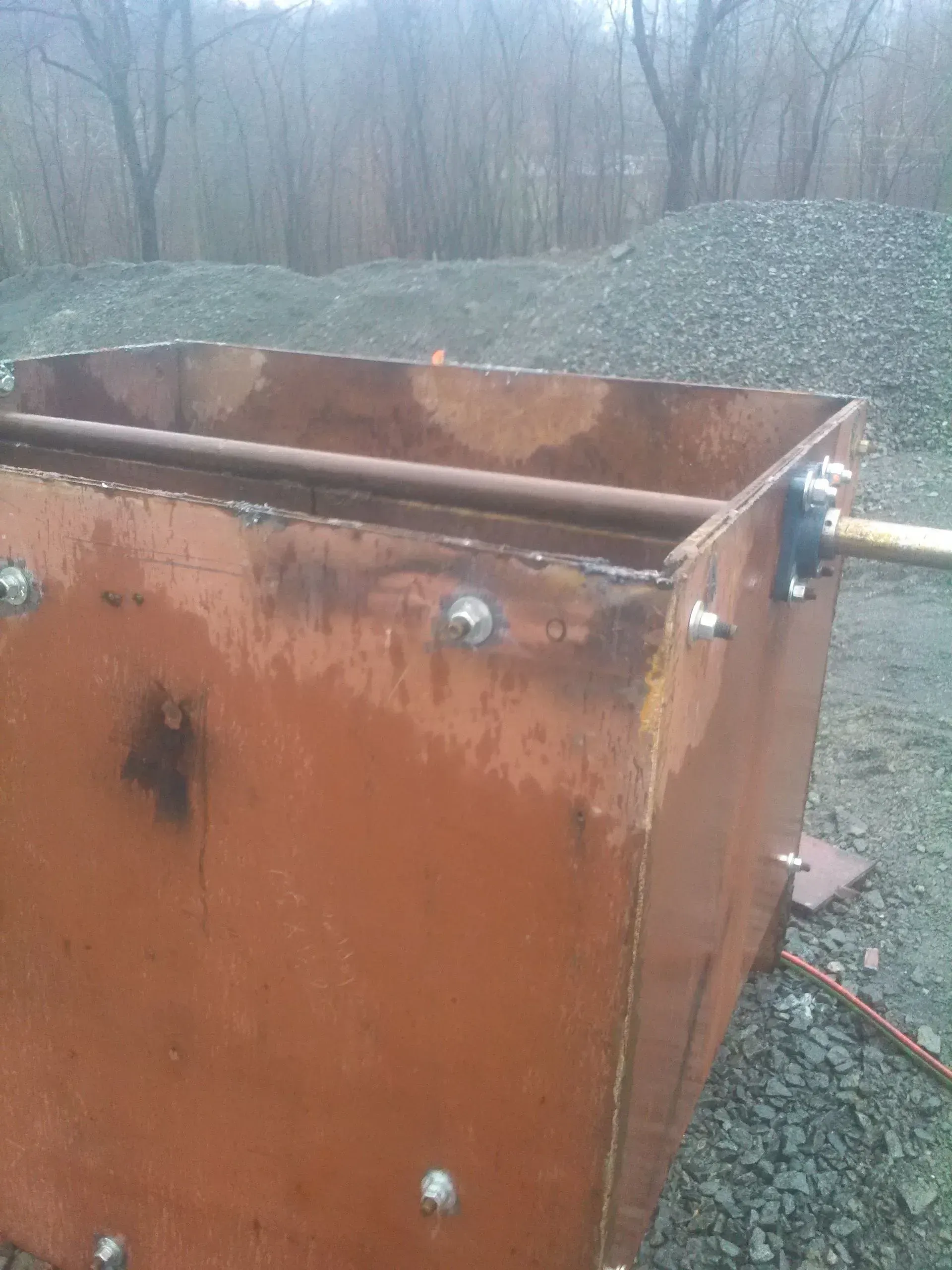 A rusty metal container is sitting on top of a gravel road.
