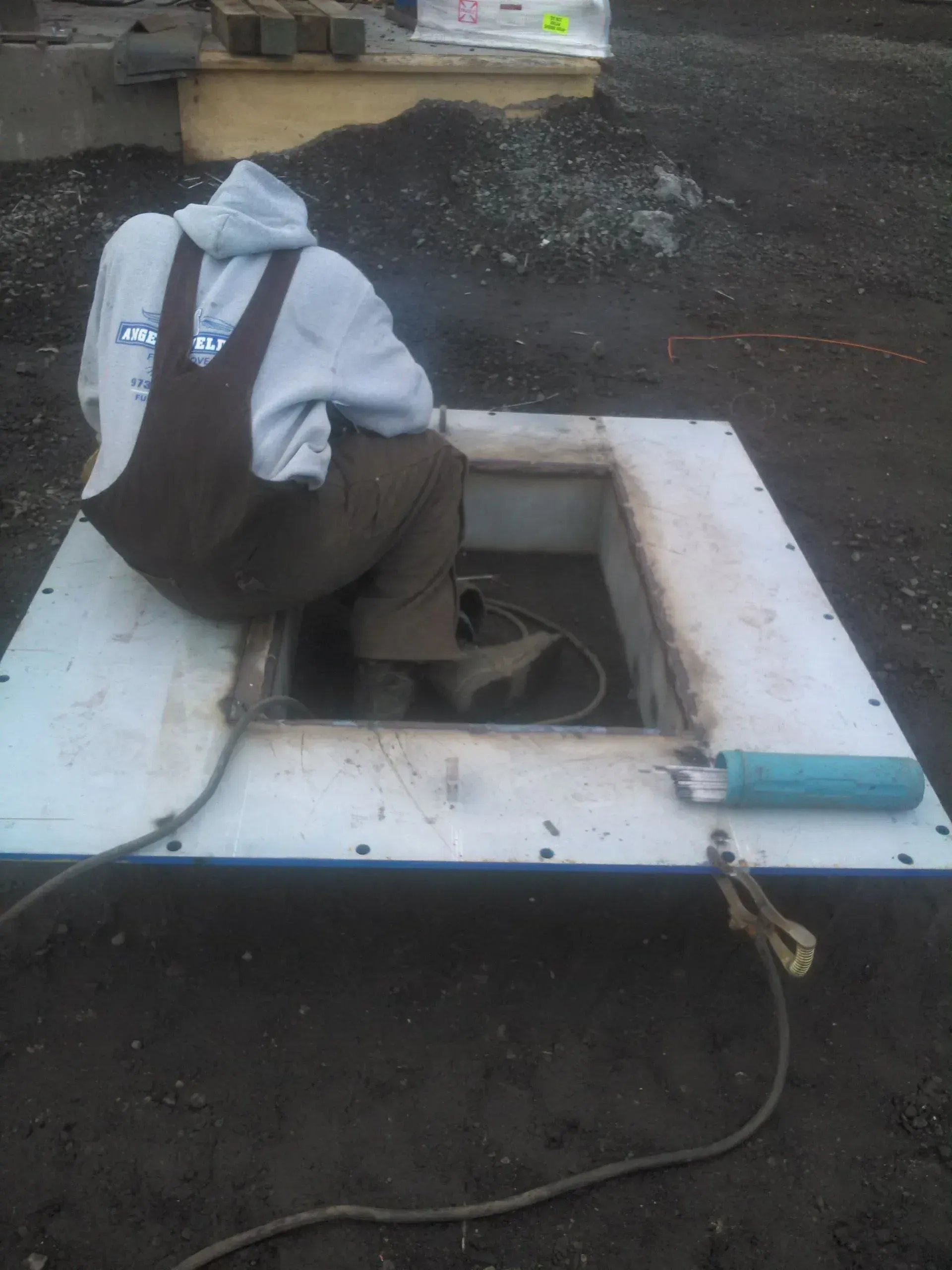 A man in overalls is sitting in a hole in the ground.