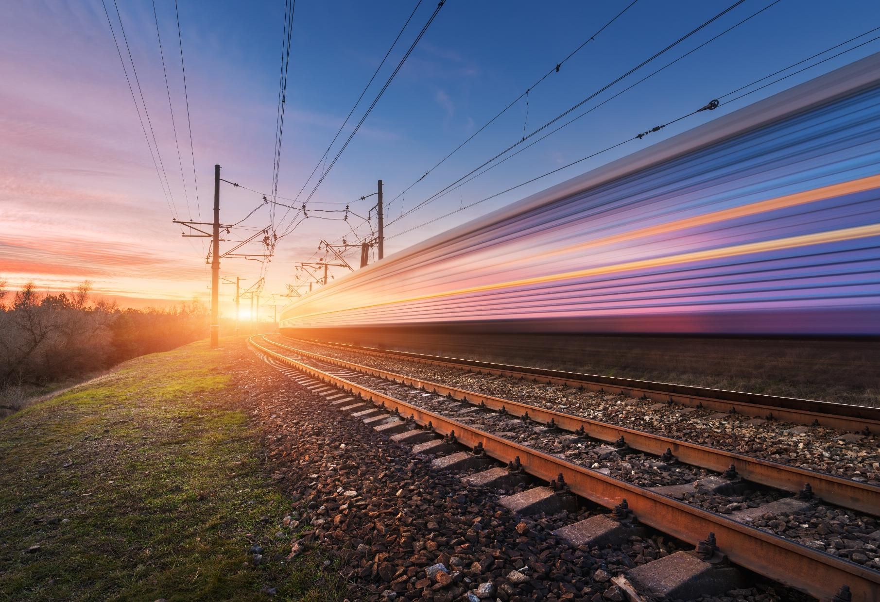 A train is going down train tracks at sunset.