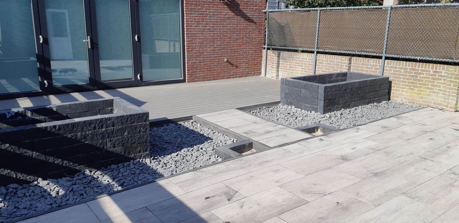 Stenen trappen en verhoogde plantenbakken naast een bakstenen gebouw op een geplaveide binnenplaats.