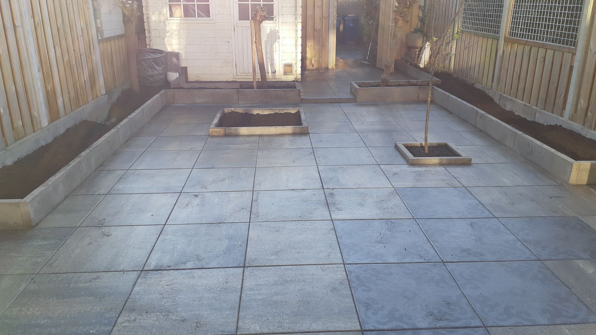 Leeg betegeld terras in de achtertuin met verhoogde plantenbakken en houten schutting.