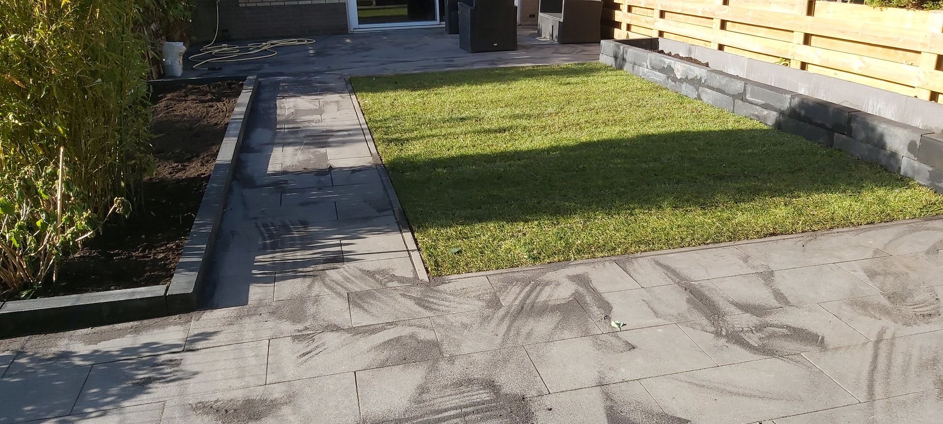 Zonnige tuin met een betonnen pad naast een groen gazon en struiken.
