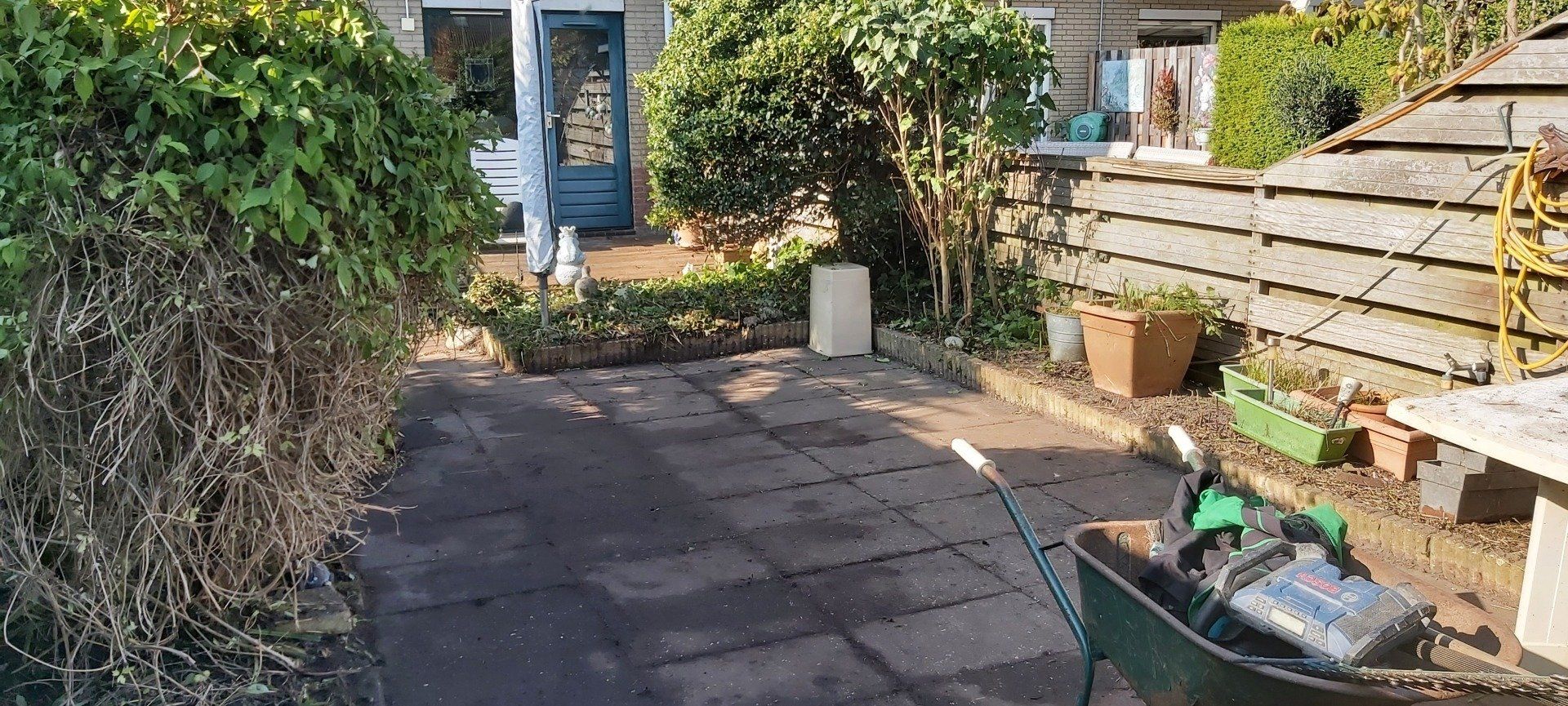 Zonnig tuinterras met bestrating, banken en planten, dat naar een deur leidt.