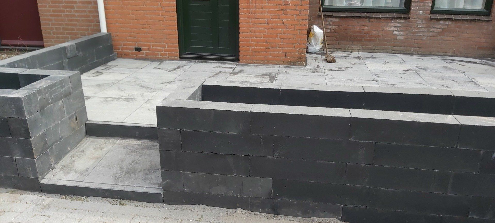 Bouwterrein met grijze betonnen muren en onafgewerkte bestrating buiten een bakstenen gebouw