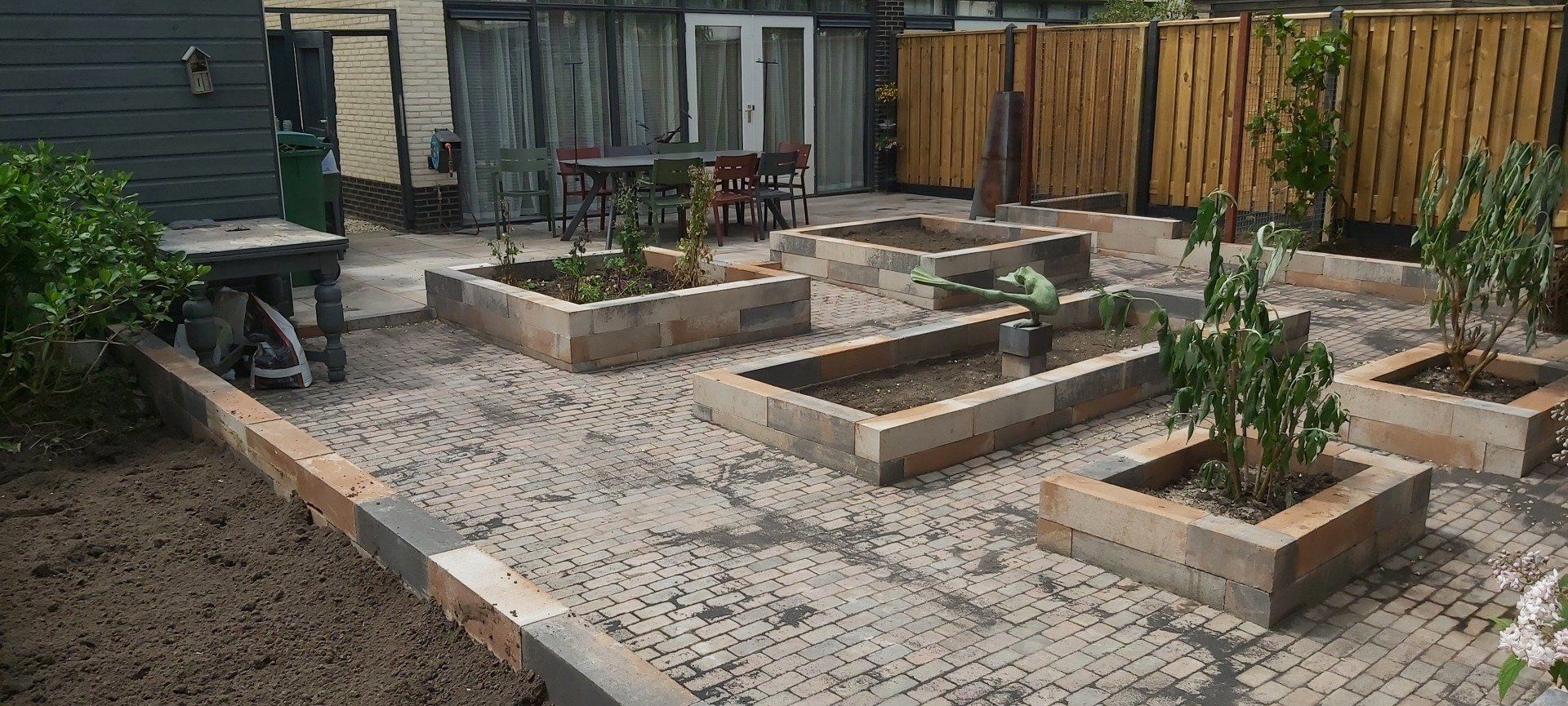 Achtertuin met verhoogde bakstenen plantenbakken, een grindpad en een houten schutting.