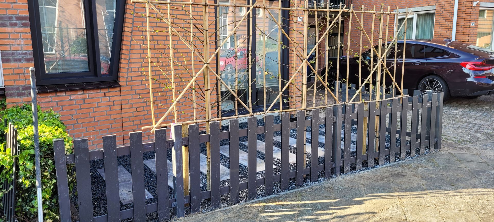 Donkere schutting voor een bakstenen gebouw met bamboestellingen en geparkeerde auto's.