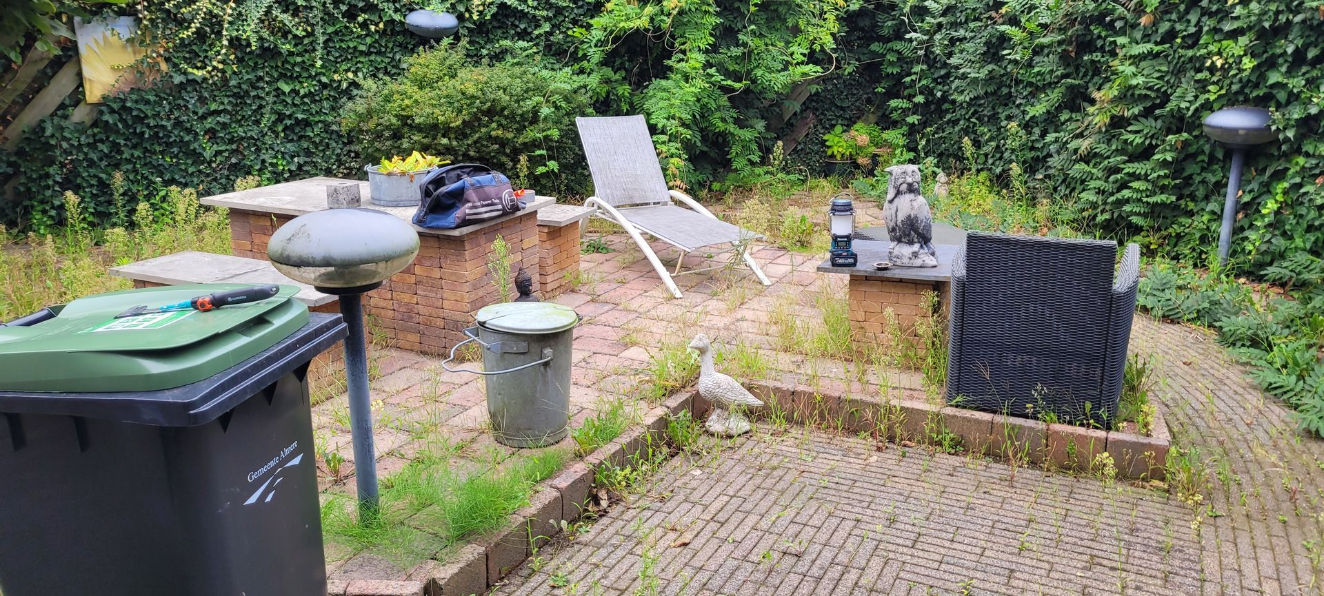 Terras in de achtertuin met barbecue, vuurkuil, ligstoelen en tuingroen.
