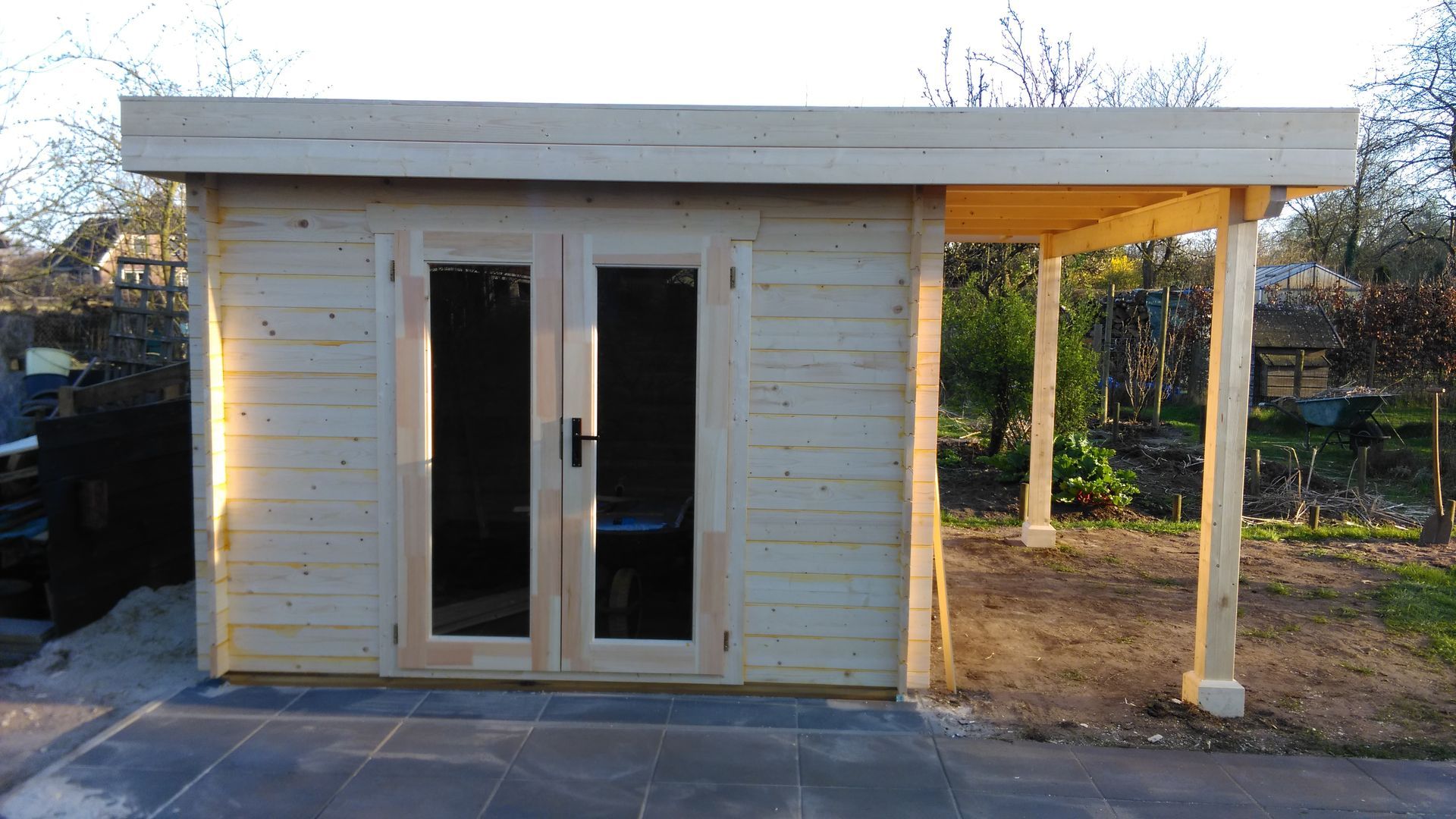 Klein wit tuinhuisje met dubbele glazen deuren en een overdekte veranda aan de zijkant in de achtertuin.