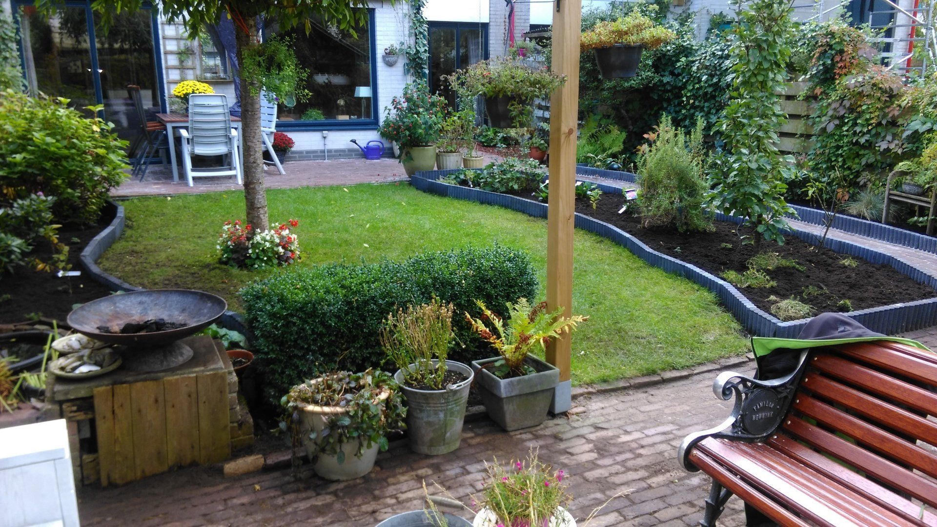 Een gebogen tuinpad met bankjes, potplanten en een kleine grasrijke binnenplaats in een parkachtige omgeving.