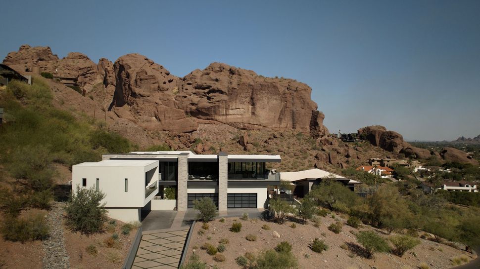 Modern white house beside rocky desert cliffs under a clear sky