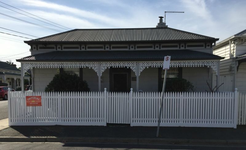 A white picket fence surrounds a house that is for sale